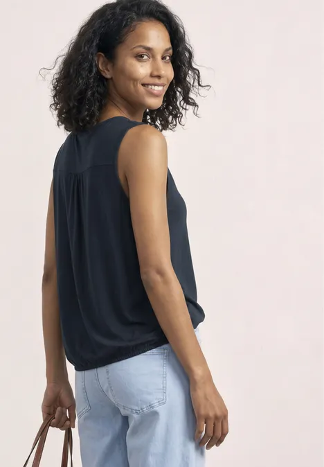 Top aus Jersey mit Elastiksaum shadowed navy Frau in schwarzem ärmellosen Top und hellblauen Jeans, hält zum seitlichen Blick eine Handtasche.