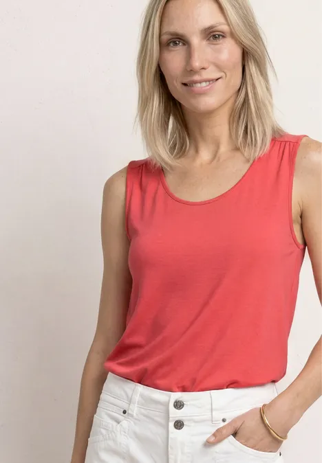 Top aus Jersey mit Elastiksaum sunset red Frau in rotem Tanktop und weißen Hosen vor einfachem Hintergrund.