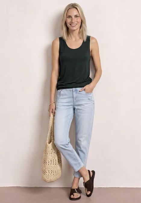 Femme en débardeur noir, jean clair et sandales noires, tenant un sac en paille tressé.