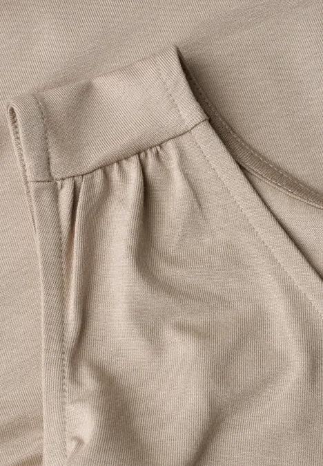 Detail van een beige kledingstuk met zak en fijne stofstructuur.