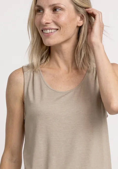 Een lachende vrouw draagt een mouwloze beige top voor een neutrale achtergrond.