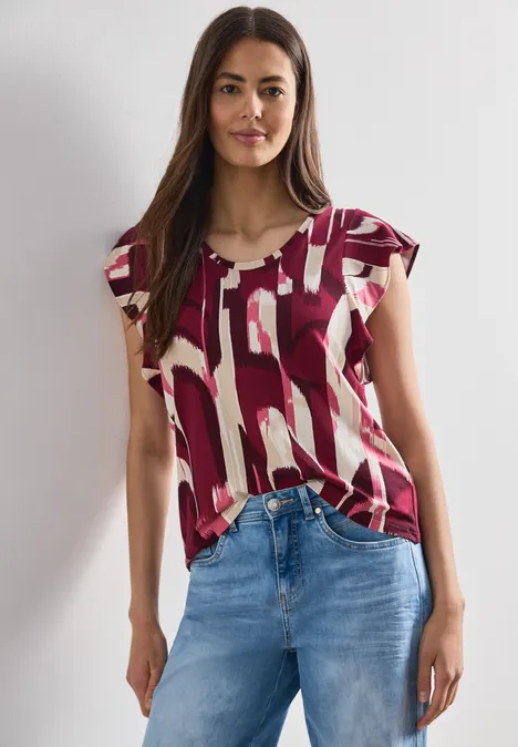Frau in gemusterter bordeaux-weißer Bluse und blauen Jeans.