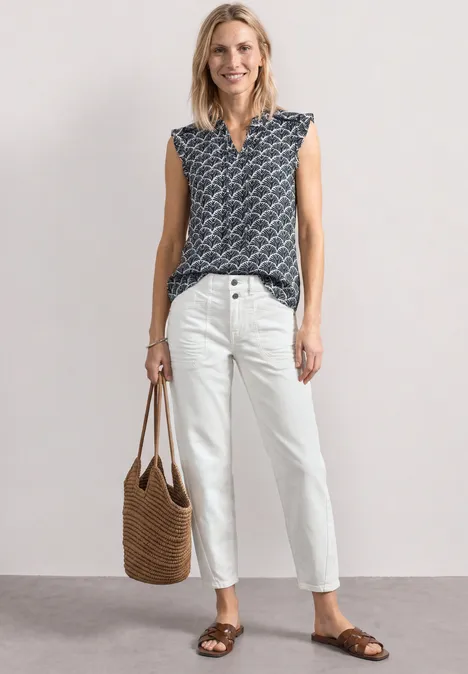 Top met verschillende texturen en gehaakte details shadowed navy Vrouw met een mouwloos topje met print, witte broek, sandalen en gevlochten tas voor neutrale achtergrond.
