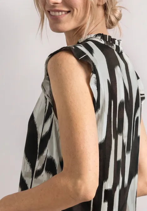 Femme en chemisier sans manches à motif noir et blanc, vue de côté, cheveux relevés en chignon.