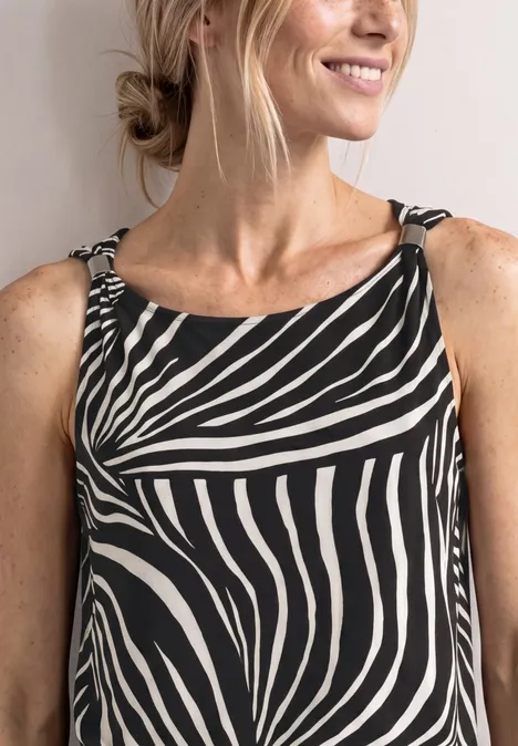 Frau mit lockerem Dutt trägt ärmelloses Zebra-Muster-Top und lächelt leicht.