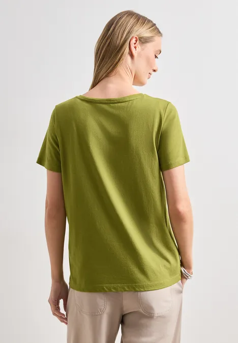 T-Shirt mit Wording Artwork shaded olive green Rückansicht einer Frau in grünem T-Shirt und beiger Hose.