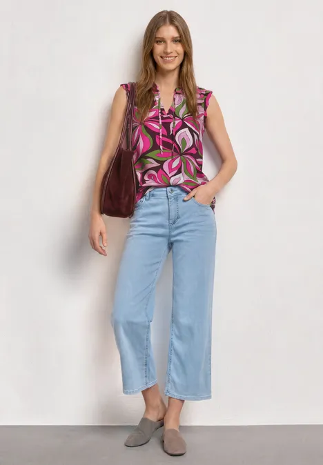 Top mit Strukturmix und Crochet-Details magenta dream Frau steht vor hellem Hintergrund, trägt geblümte Bluse, hellblaue Cropped-Jeans, graue Loafers und braune Tasche.