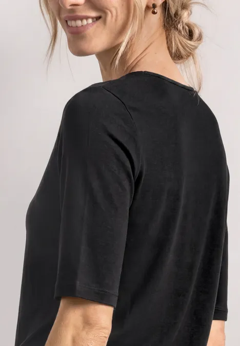 Vrouw van achteren in een zwart shirt met halflange mouwen, losse knot en subtiele oorbel.