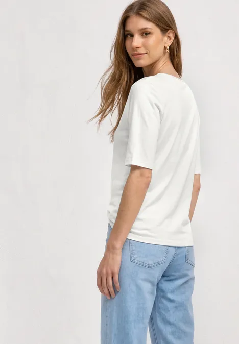 Vrouw van achteren in een wit t-shirt en blauwe spijkerbroek tegen lichte achtergrond.
