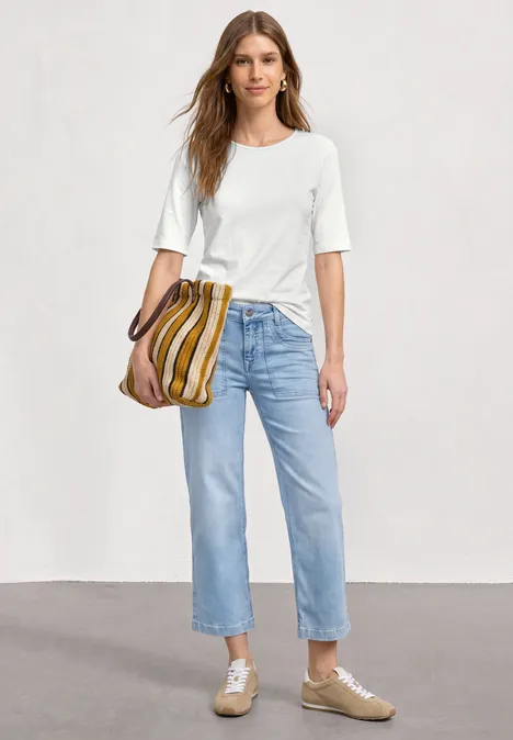 Een vrouw draagt een wit t-shirt, lichtblauwe spijkerbroek, beige schoenen en een gestreepte tas.