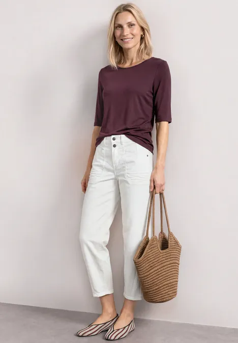 Basic Shirt met ronde hals in Unifarbe rustic rouge Vrouw in paars 3/4-mouwshirt, witte high waist jeans, zwart-witte ballerina’s en gevlochten strandtas.