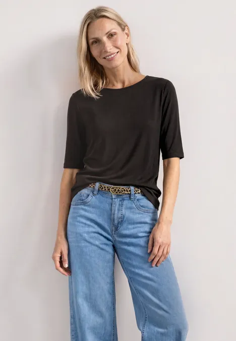 Basic Shirt met ronde hals in Unifarbe black coffee Vrouw draagt zwart t-shirt, lichtblauwe losse jeans en een luipaardriem voor een witte achtergrond.