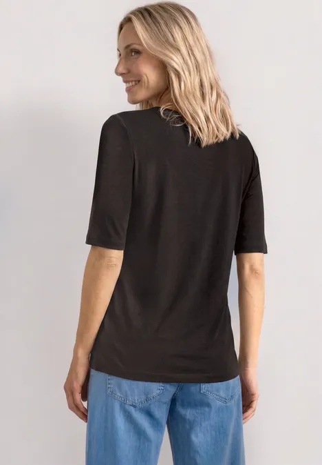 Basic Shirt met ronde hals in Unifarbe black coffee Persoon van achteren in zwart t-shirt, blauwe jeans en schouderlang blond haar.