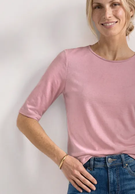 Vrouw draagt een lichtroze shirt met halflange mouwen, nonchalant ingestopt in een blauwe jeans.
