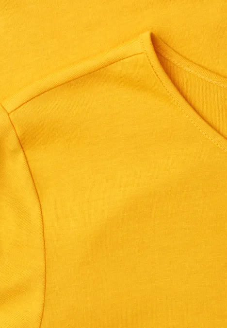 Close-up van een geel T-shirt met zichtbare naad bij mouw en hals.