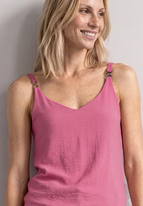 Lächelnde Frau mit blonden Haaren trägt rosa Top mit Spaghettiträgern