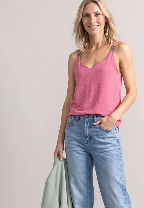 Eine lächelnde Frau in rosa Top und Jeans, hält eine hellgrüne Jacke in der Hand.