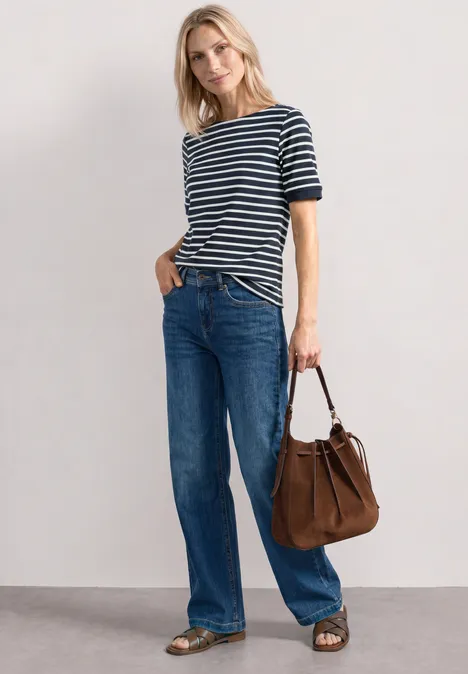 Frau trägt gestreiften Pullover, weite Jeans, braunen Shopper und Sandalen vor neutralem Hintergrund.
