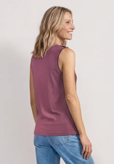 Rückansicht einer Frau mit blondem Haar in einem ärmellosen violetten Top und blauer Jeans.