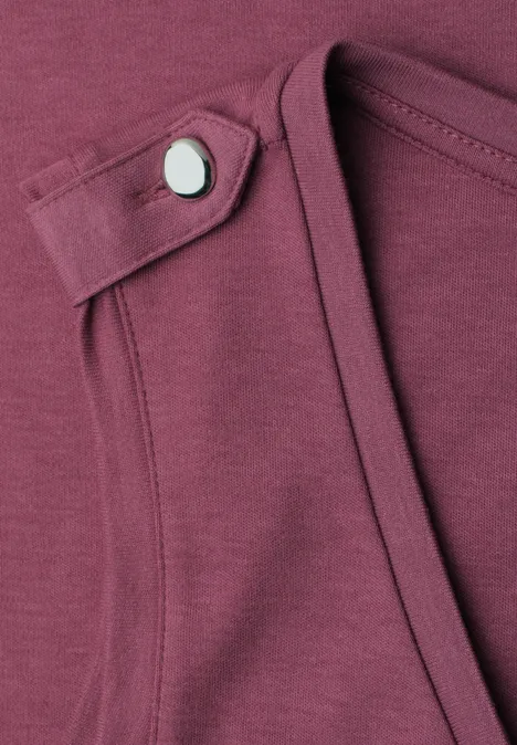 Nahaufnahme eines bordeauxfarbenen Shirts mit schmalem Riegel und silbernem Druckknopf am Ausschnitt.