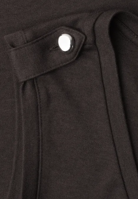 Nahaufnahme eines schwarzen Kleidungsstücks mit aufgesetzter Tasche und sichtbarem Druckknopf