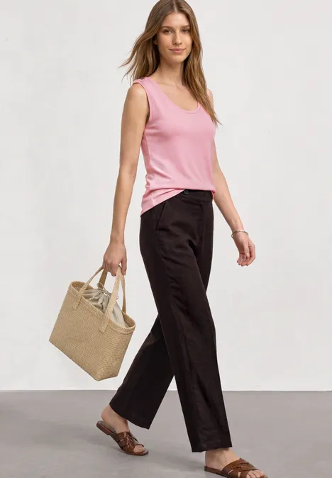 Frau in schwarzer Hose, pinkem Top, Sandalen und mit beiger Tasche.
