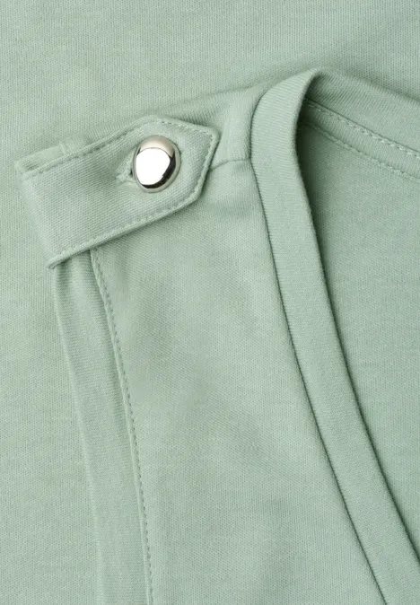 Gros plan sur un tissu vert menthe avec sangle, couture et bouton-pression argenté.