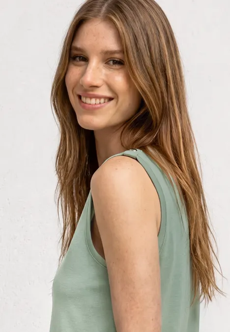 Portrait de profil d’une jeune femme aux longs cheveux bruns portant un haut vert sans manches devant un fond clair.