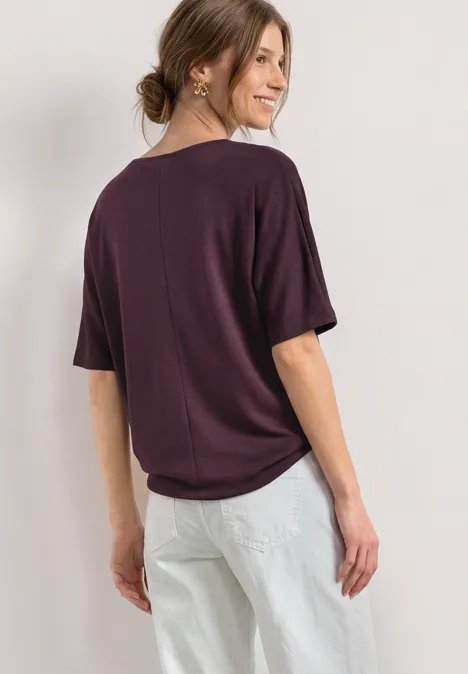 Basic Shirt mit Boat Neck und Elastikbund rustic rouge Dame in locker sitzendem dunkelviolettem T-Shirt und heller Hose von hinten fotografiert.