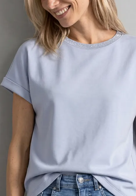 Eine lächelnde Frau in einem hellblauen T-Shirt und Jeans.
