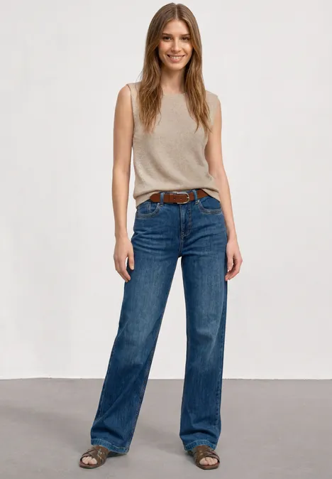 Top mit Rundhals und Glitzer clay sand Frau mit langem Haar in beige ärmellosem Top, weiten blauen Jeans und Sandalen vor hellem Hintergrund.