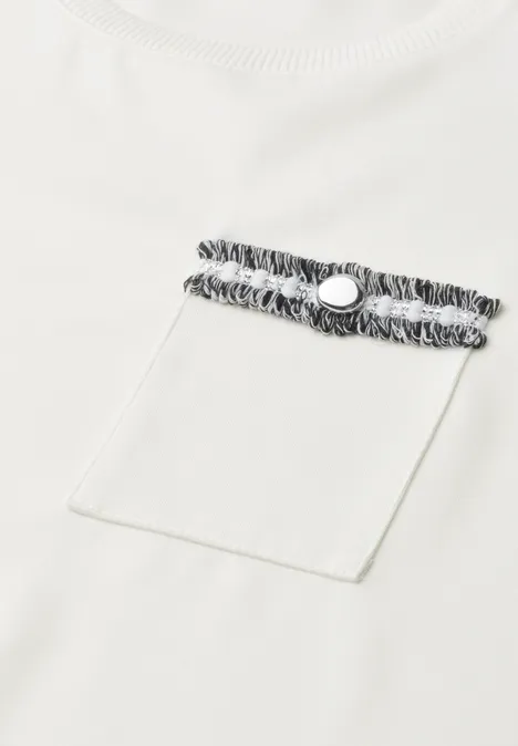 Close-up van een wit T-shirt met borstzak, versierd met een zwart-wit gestreept band en drukknop.