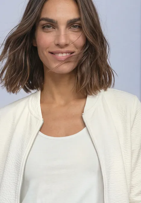 3/4-Arm Jacke mit Zipper und Struktur off white Frau mit schulterlangen braunen Haaren lächelt in weißem Top und hellem Cardigan vor hellem Hintergrund.