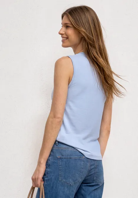 Top in Silk-Look met col whispery blue Vrouw van achteren in lichtblauw mouwloos topje en blauwe jeans voor witte muur.