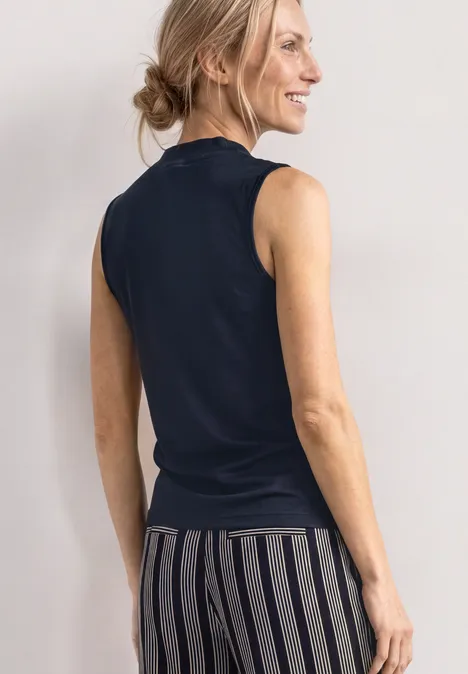 Top in Silk-Look met coltrui darkest blue Een vrouw van achteren in een zwarte mouwloze top en een gestreepte broek.
