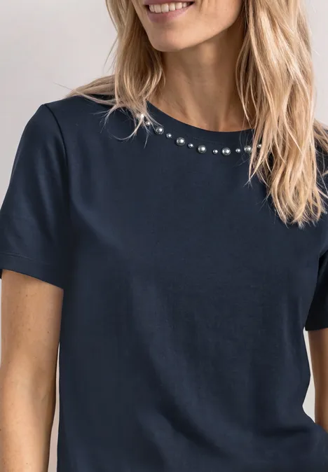 Femme blonde en tee-shirt bleu marine à manches courtes, col rond orné de petits strass.