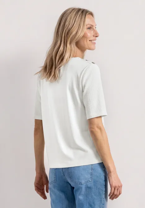 Frau von hinten, trägt weißes T-Shirt und blaue Jeans, vor hellem Hintergrund.