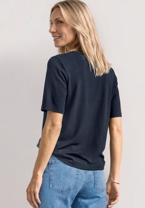Frau mit blonden Haaren von hinten, trägt schwarzes T-Shirt und blaue Jeans.