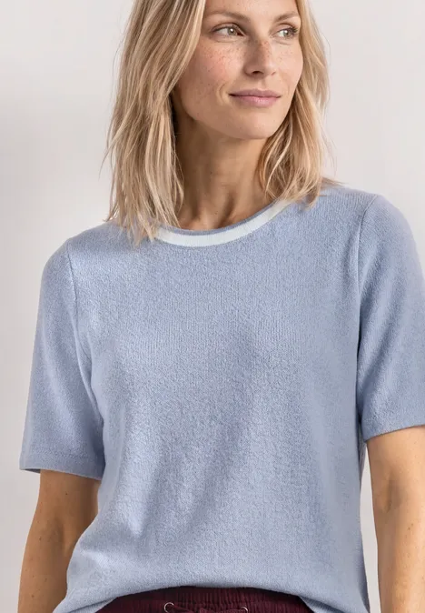 Vrouw in lichtblauw T-shirt met korte mouwen en bordeauxrode rok voor lichte achtergrond.