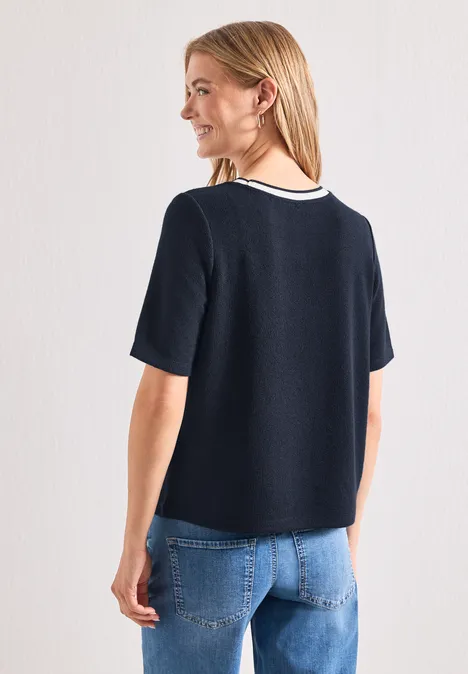 Vrouw van achteren in een donkerblauw T-shirt met witte kraag en een blauwe spijkerbroek.