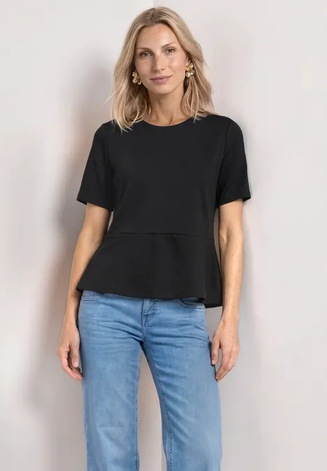 T-Shirt mit Rundhals und Volant-Detail Black Frau trägt schwarzen T-Shirt und blaue Jeans, steht frontal vor neutralem Hintergrund.