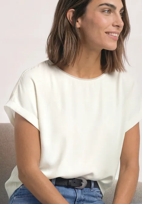 2-in-1 Shirt aus Chiffon mit Boat Neck off white Lächelnde Frau in schlichtem weißen T-Shirt mit umgeschlagenen Ärmeln, Jeans und Gürtel.