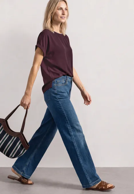 Eine Frau in Jeans und bordeauxrotem T-Shirt mit gestreifter Tasche, die selbstbewusst geht.