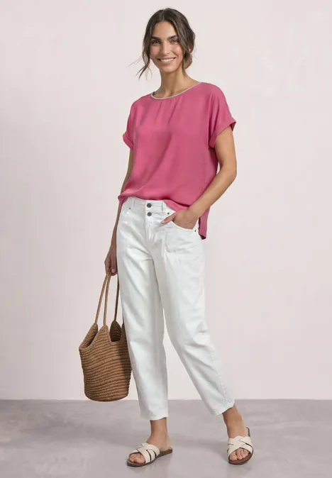 2-in-1 Shirt aus Chiffon mit Boat Neck blush berry Frau trägt pinke Bluse, weiße Jeans, Basttasche und weiße Sandalen vor hellem Hintergrund.