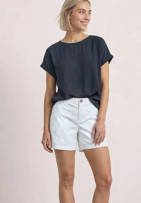 Eine Frau in marineblauem T-Shirt und weißen Shorts vor hellem Hintergrund.