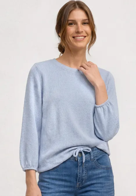 3/4-Arm Shirt mit Rundhals im Strick-Look whispery blue mel. Person trägt hellblauen Strickpullover mit 3/4-Ärmeln und Bindeband, kombiniert mit blauen Jeans.