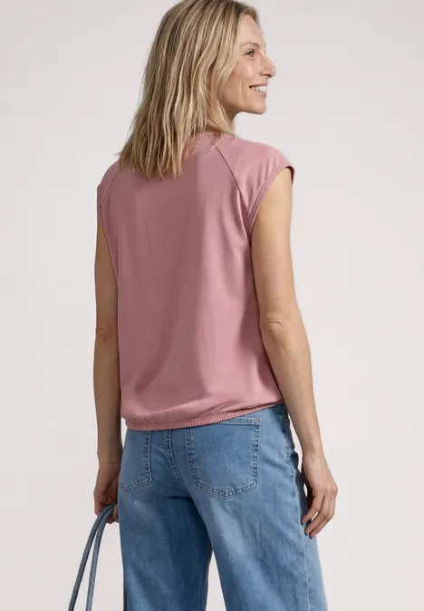 Achteraanzicht van een vrouw in een roze top en blauwe jeans, met een tas in haar hand.