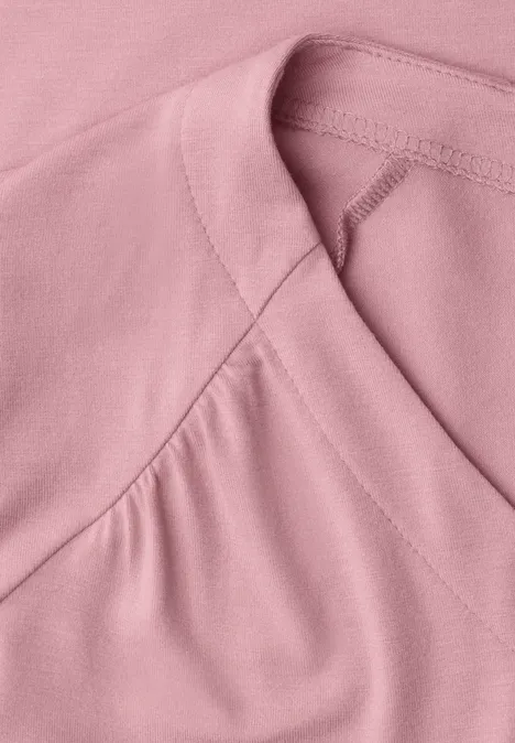 Close-up van een roze shirt met fijne stiknaden bij de halslijn.