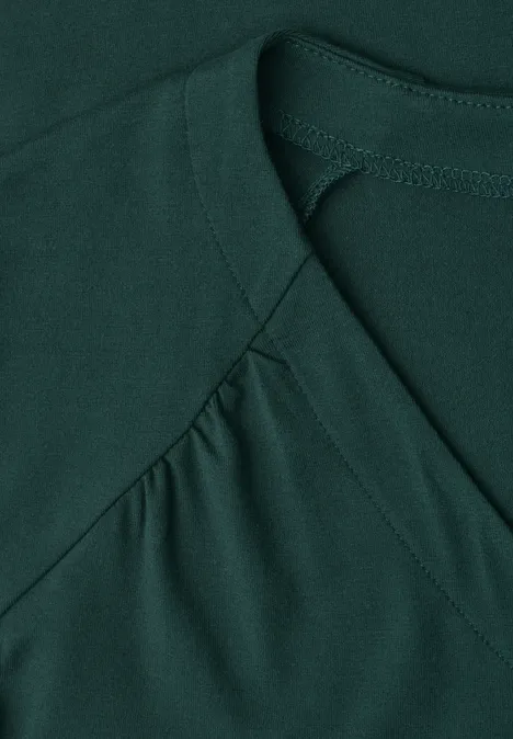 Close-up van een donkergroene top met V-vormige naad bij de hals.