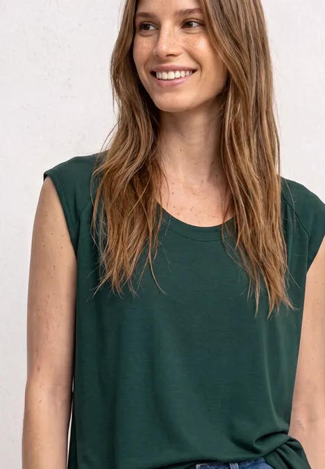 Een glimlachende vrouw met lang haar draagt een mouwloos, donkergroen topje.